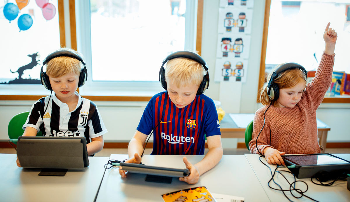 2 barn ser på iPad, en trekker opp hånda