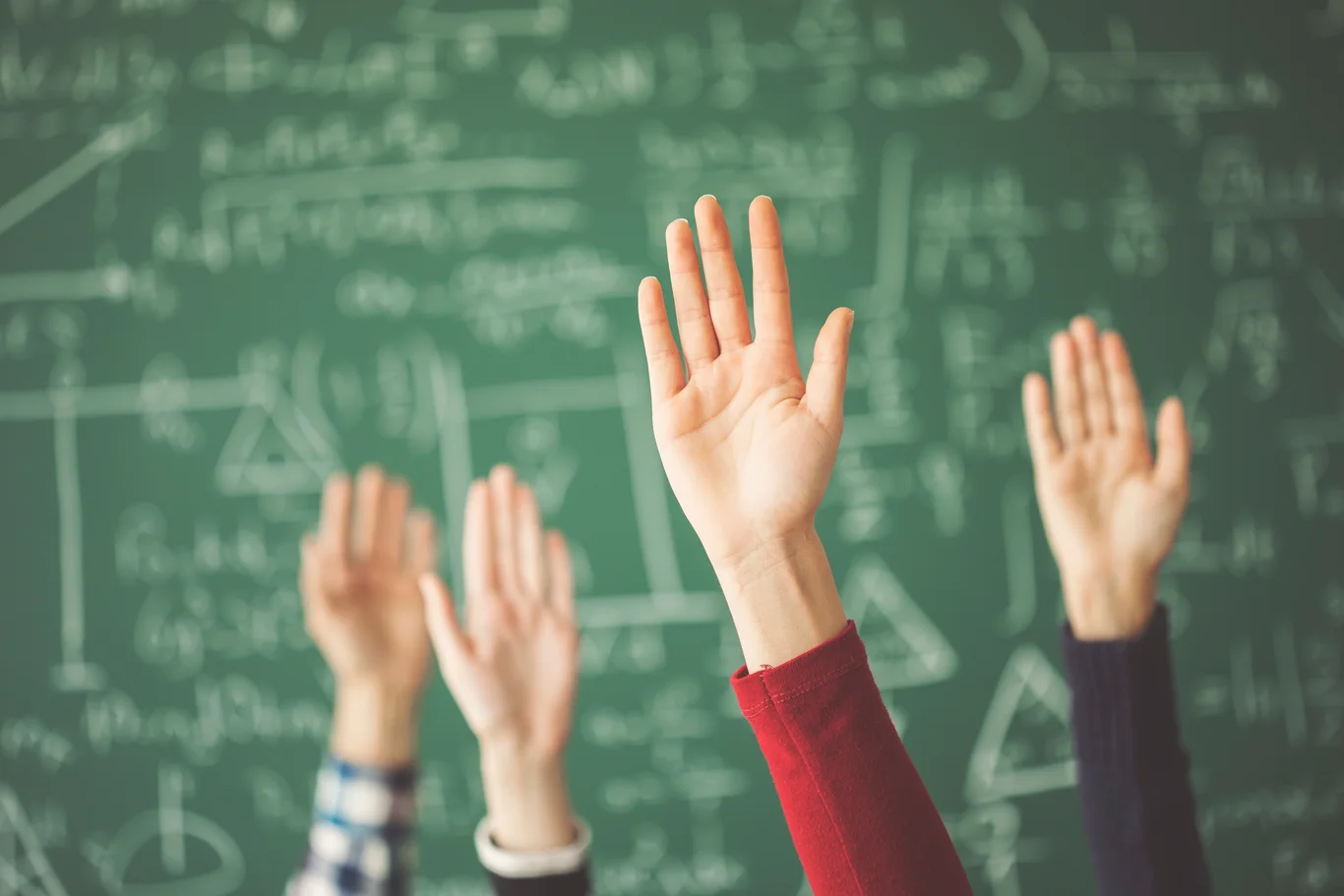 En rekke hender som holdes opp foran en tavle med matematikk skriblerier