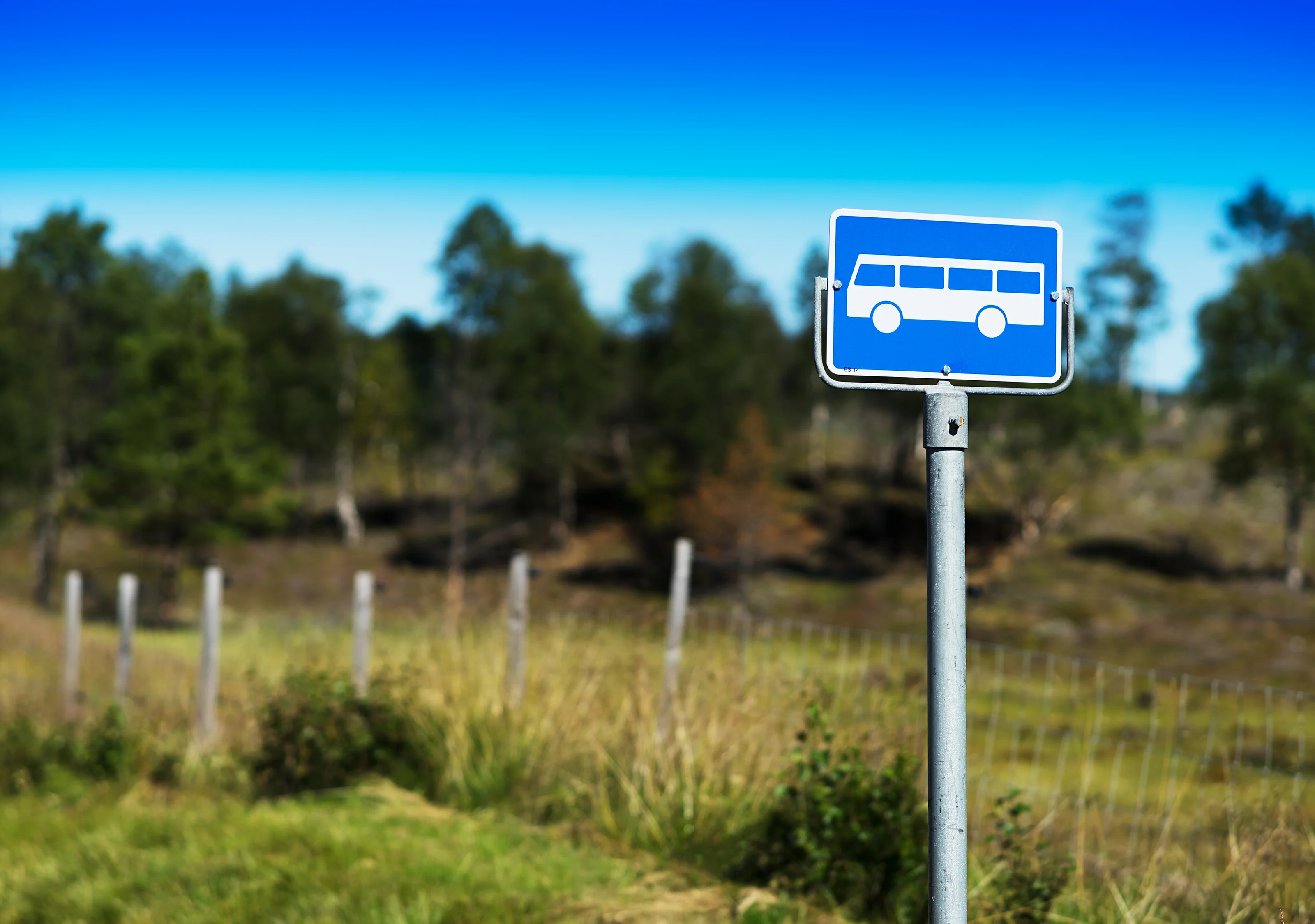 Et blått busskilt mot skyfri himmel plassert på et øde sted, omgitt av typisk norsk natur.