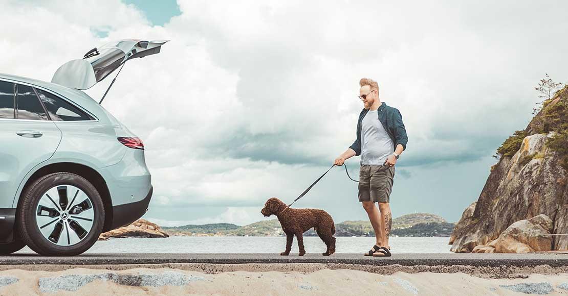 Mann lufter en hund bak en Mercedes-Benz EQC