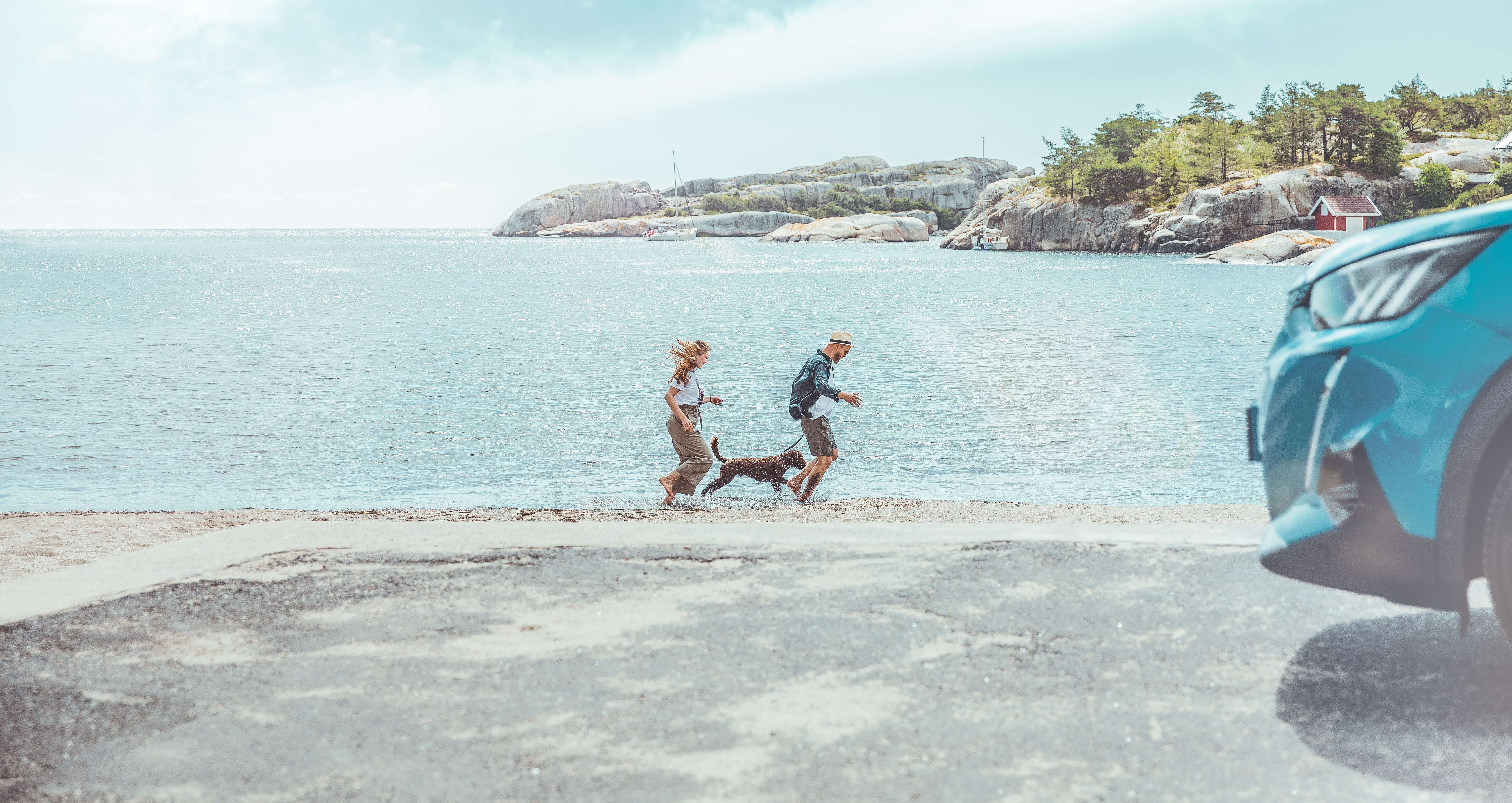 To mennesker og en hund på en strand med bil i forgrunnen