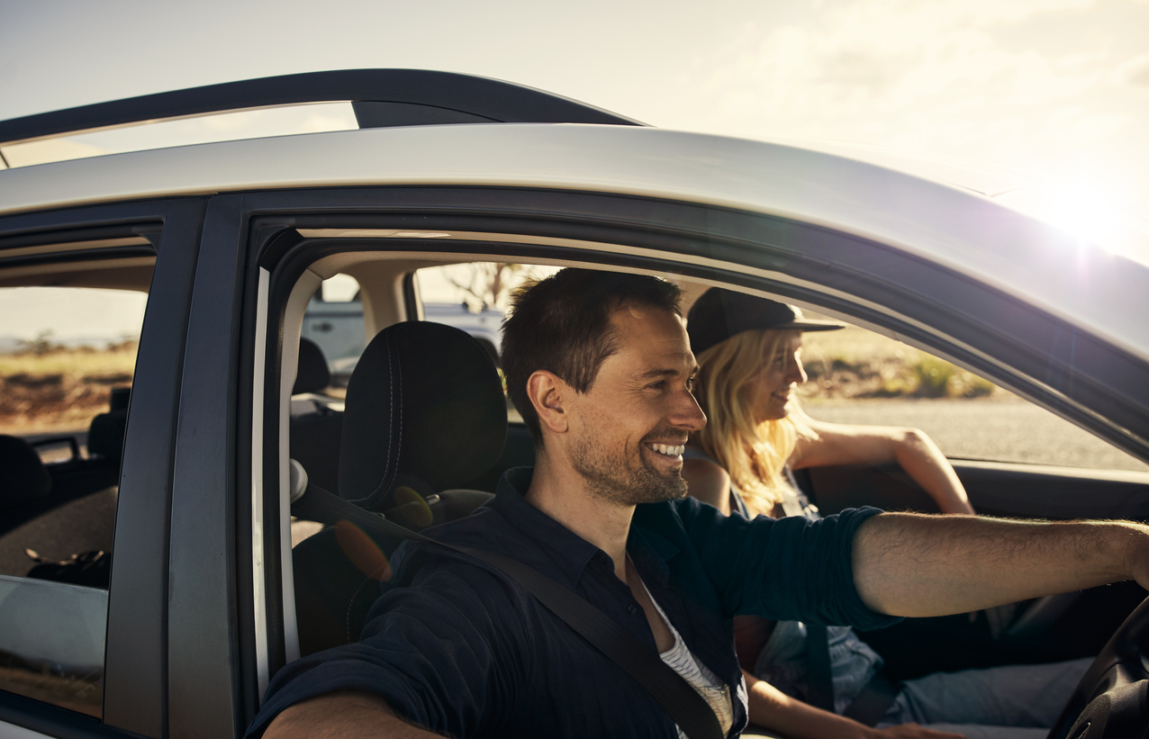 Par som smiler mens de kjører bil i solskinn