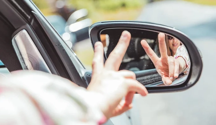 To fingre, formet som peace-tegn, som holdes opp i et bilspeil.