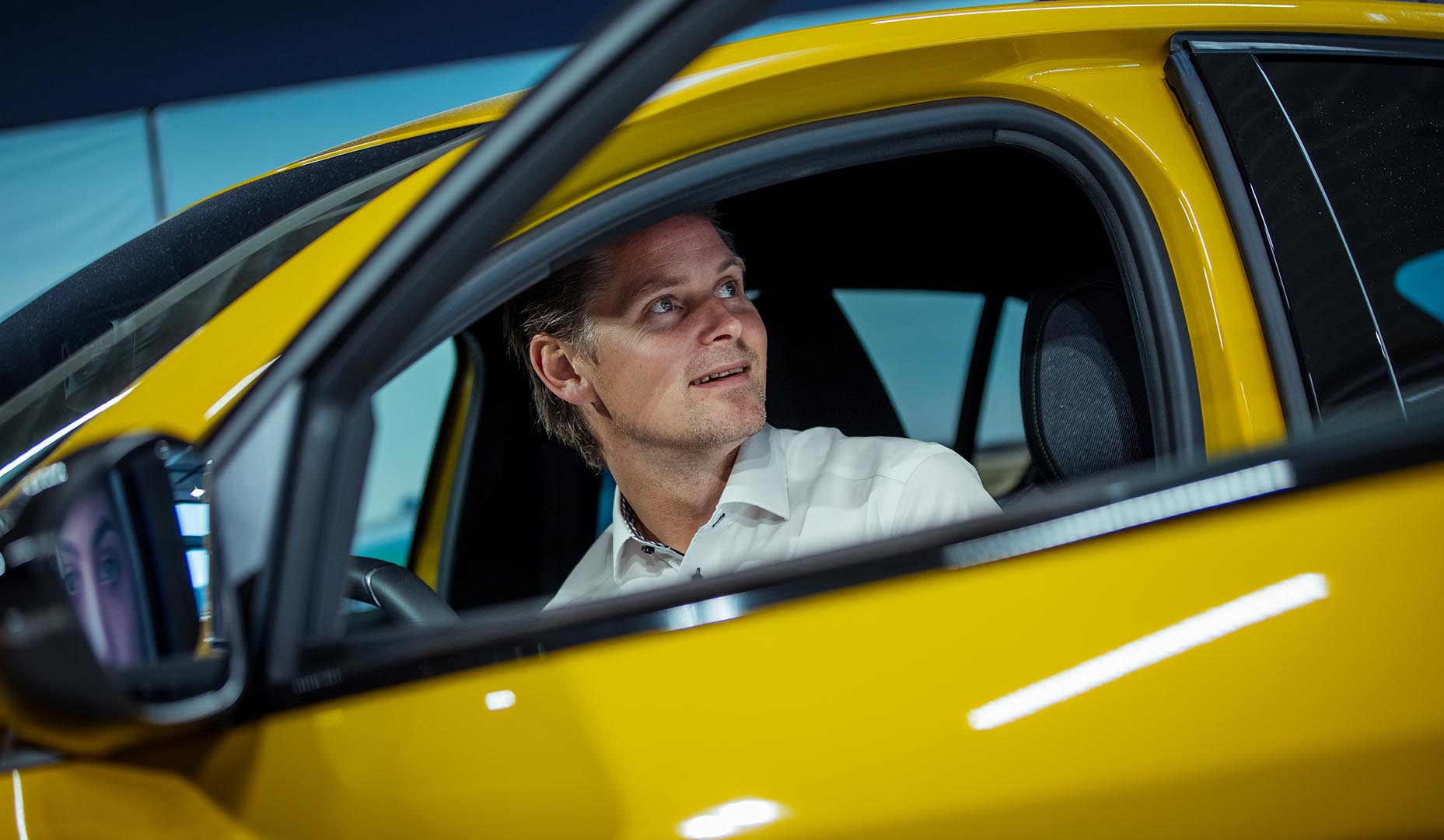 Mann sitter i en gul bil med døren åpen og kikker ut