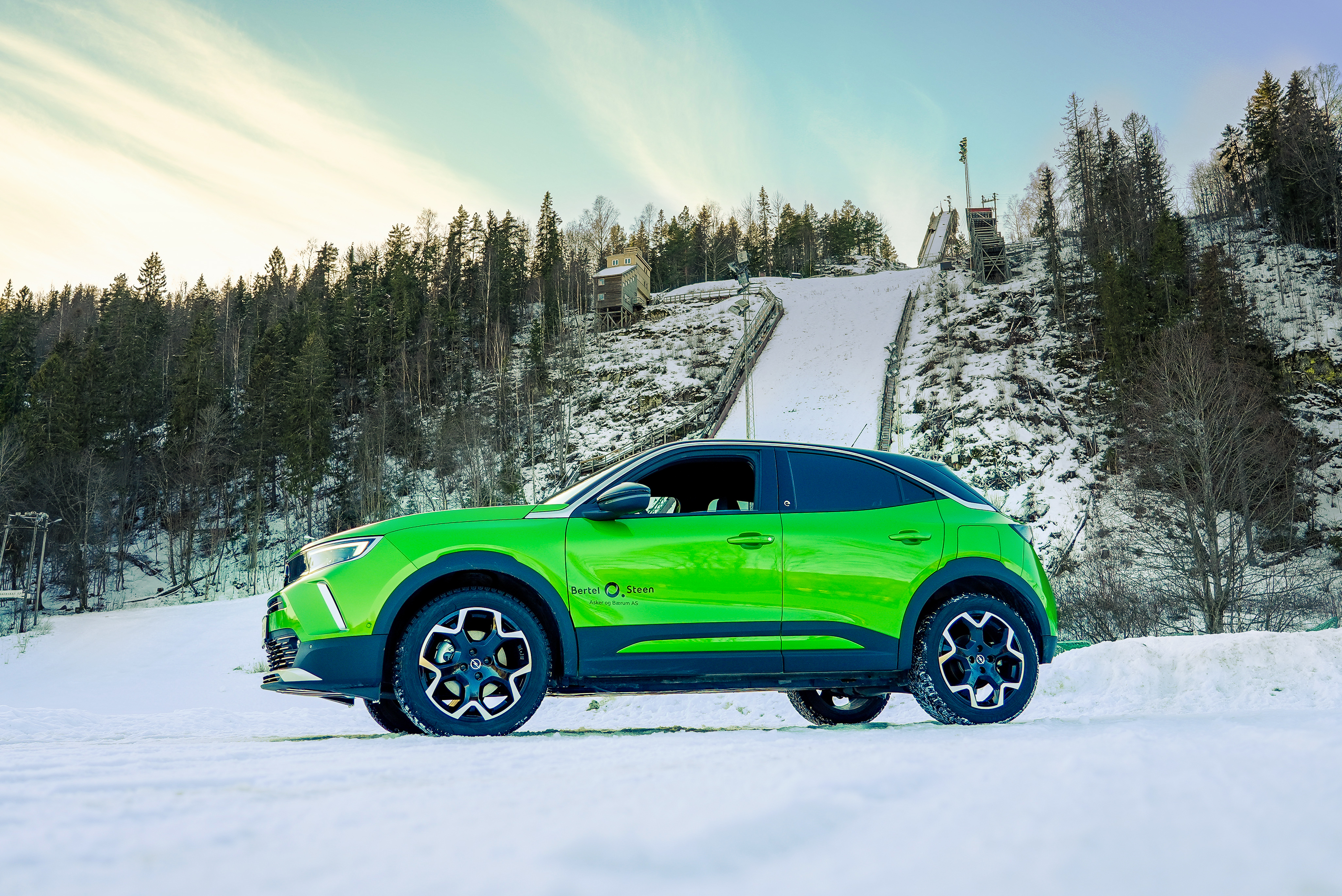 Grønn Opel Mokka-e står oppstilt under nordiske forhold i en hoppbakke på snødekt underlag.