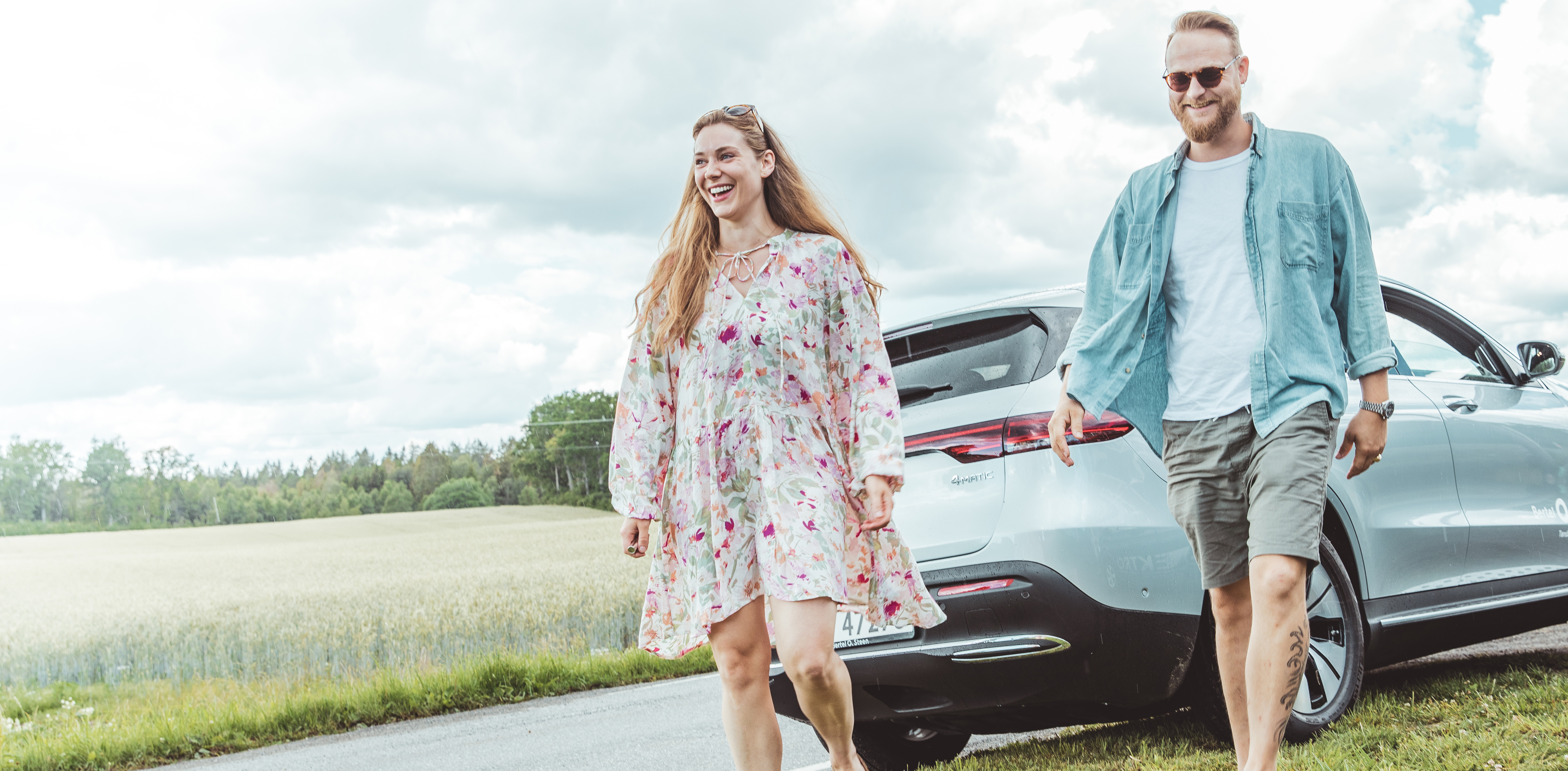 Smilende par i sommerlige omgivelser med Mercedes EQC i bakgrunnen