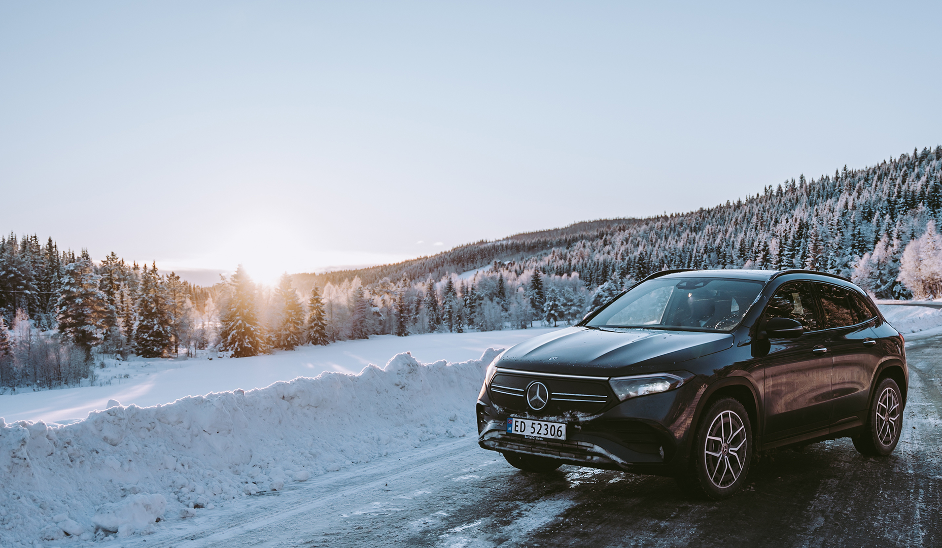 EQA fra Mercedes-EQ står parkert i vinterlandskap med solnedgang i horisonten.