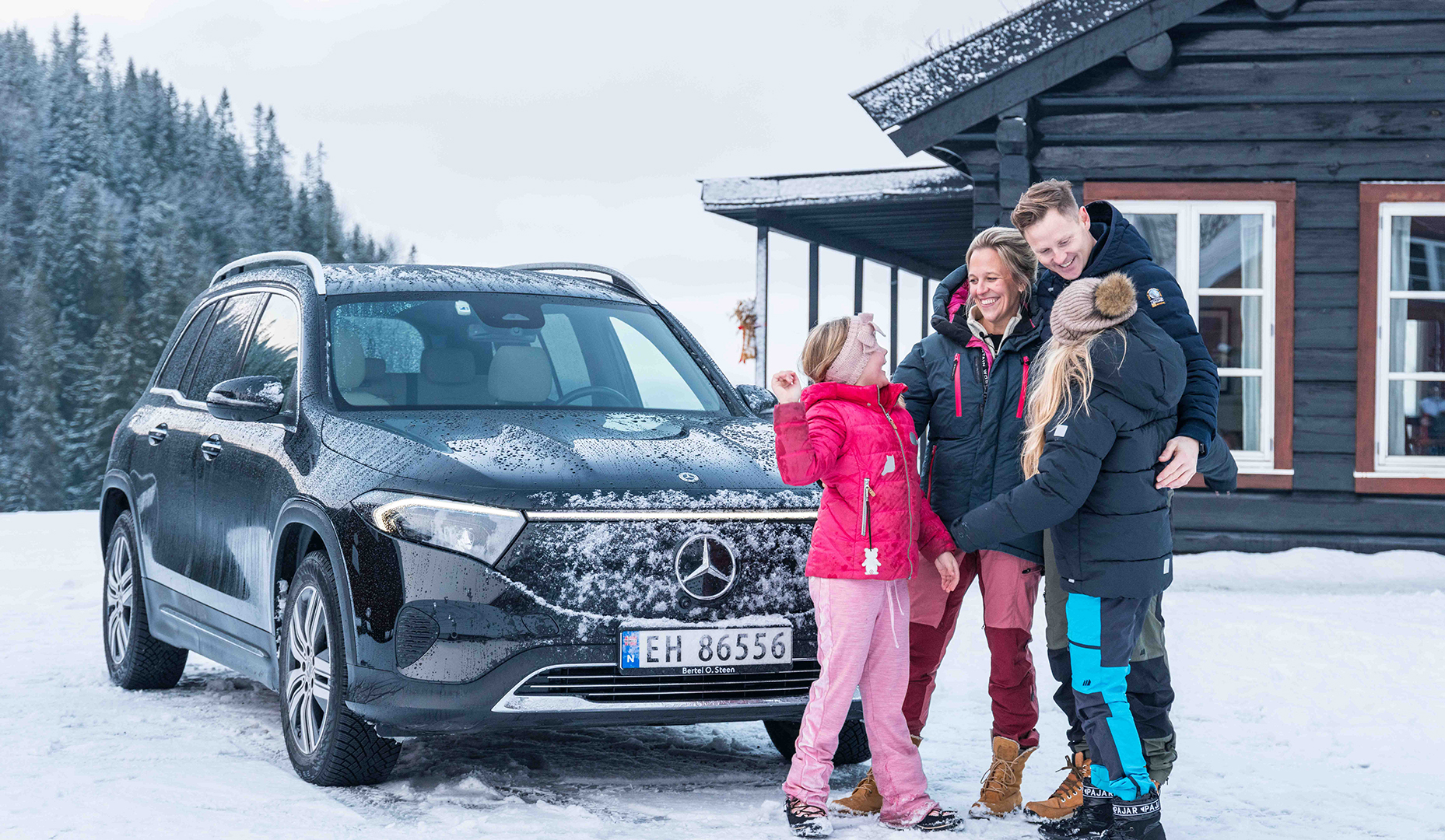 Familie med to barn står foran Mercedes-Benz EQB og en hytte i vinterlandskap