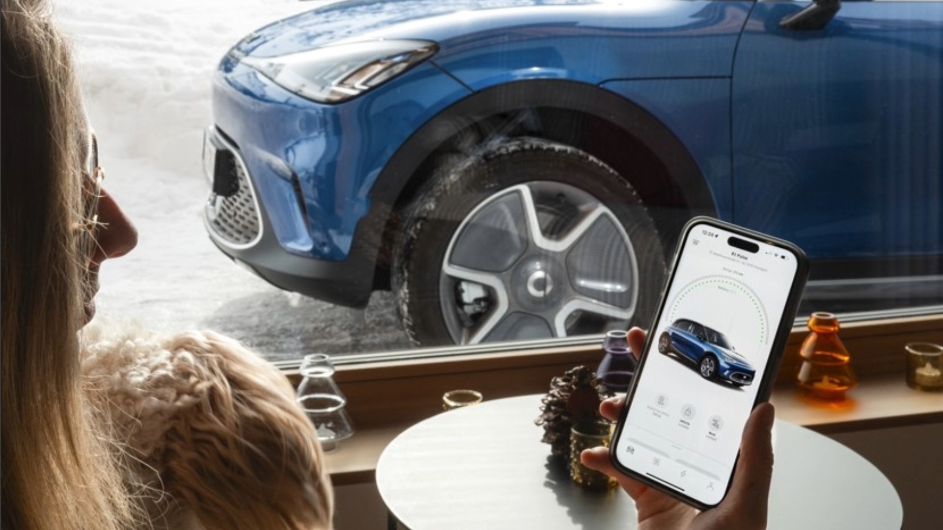 Person bruker Hello smart-appen for å sende ladestasjon til bilen, mens en blå smart står parkert ute på vinteren