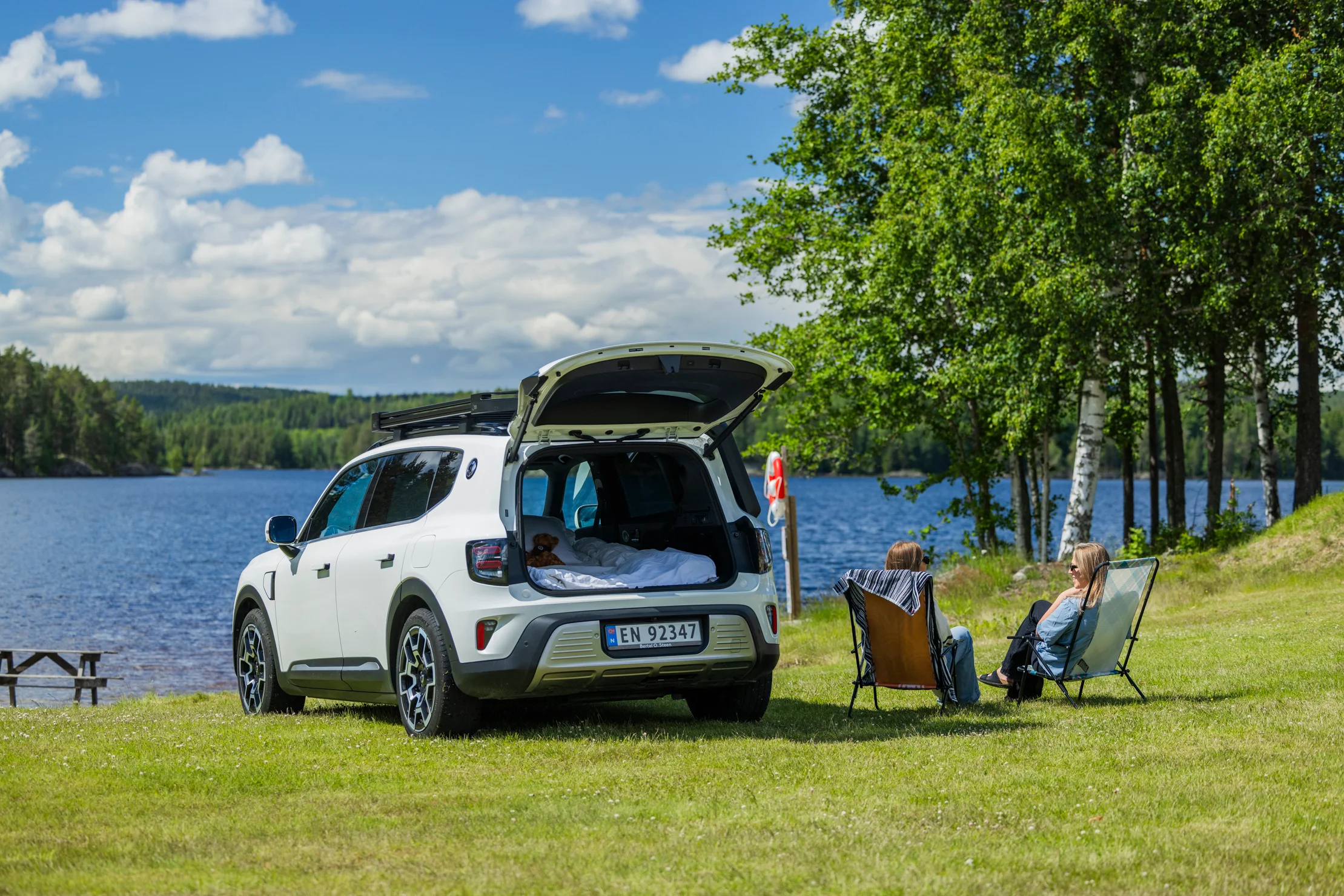 smart #5 parkert ved et vann med åpent bagasjerom og to personer i campingstoler