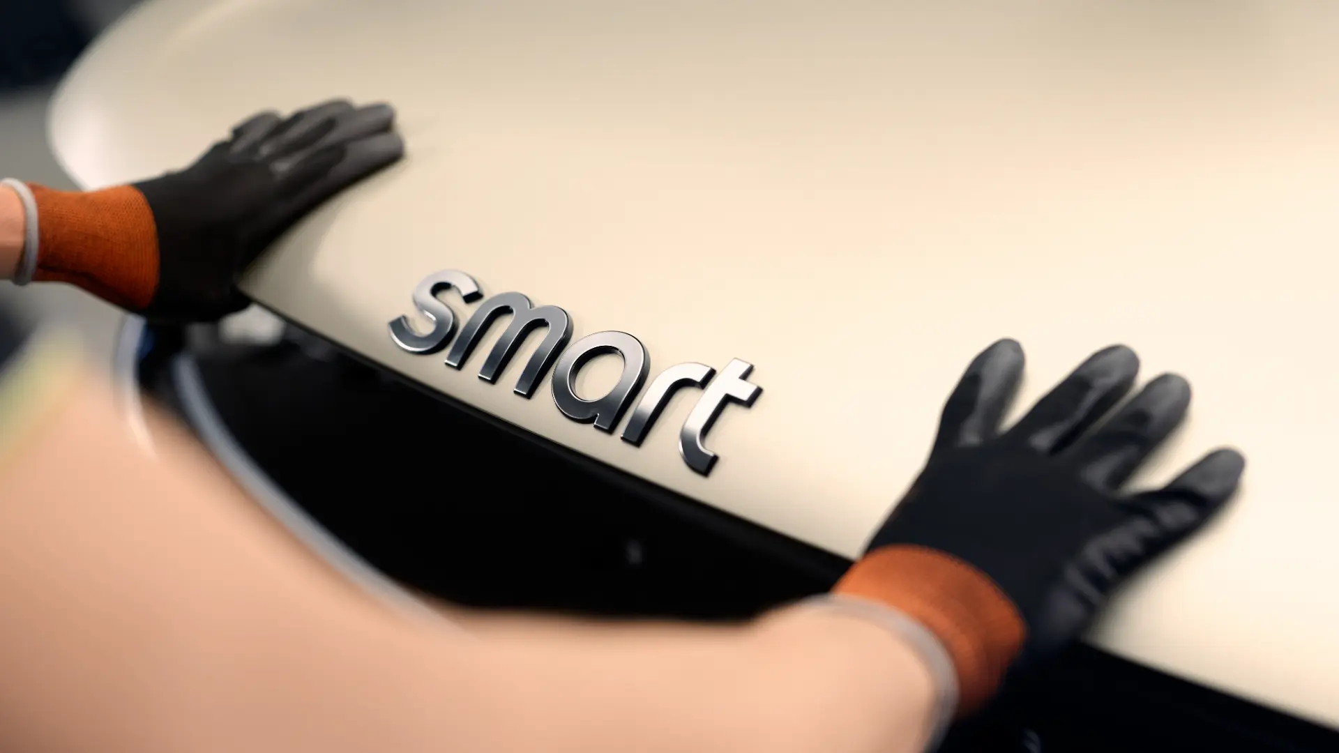 Nærbilde av smart-logo på en smart-bil med hanskekledde hender