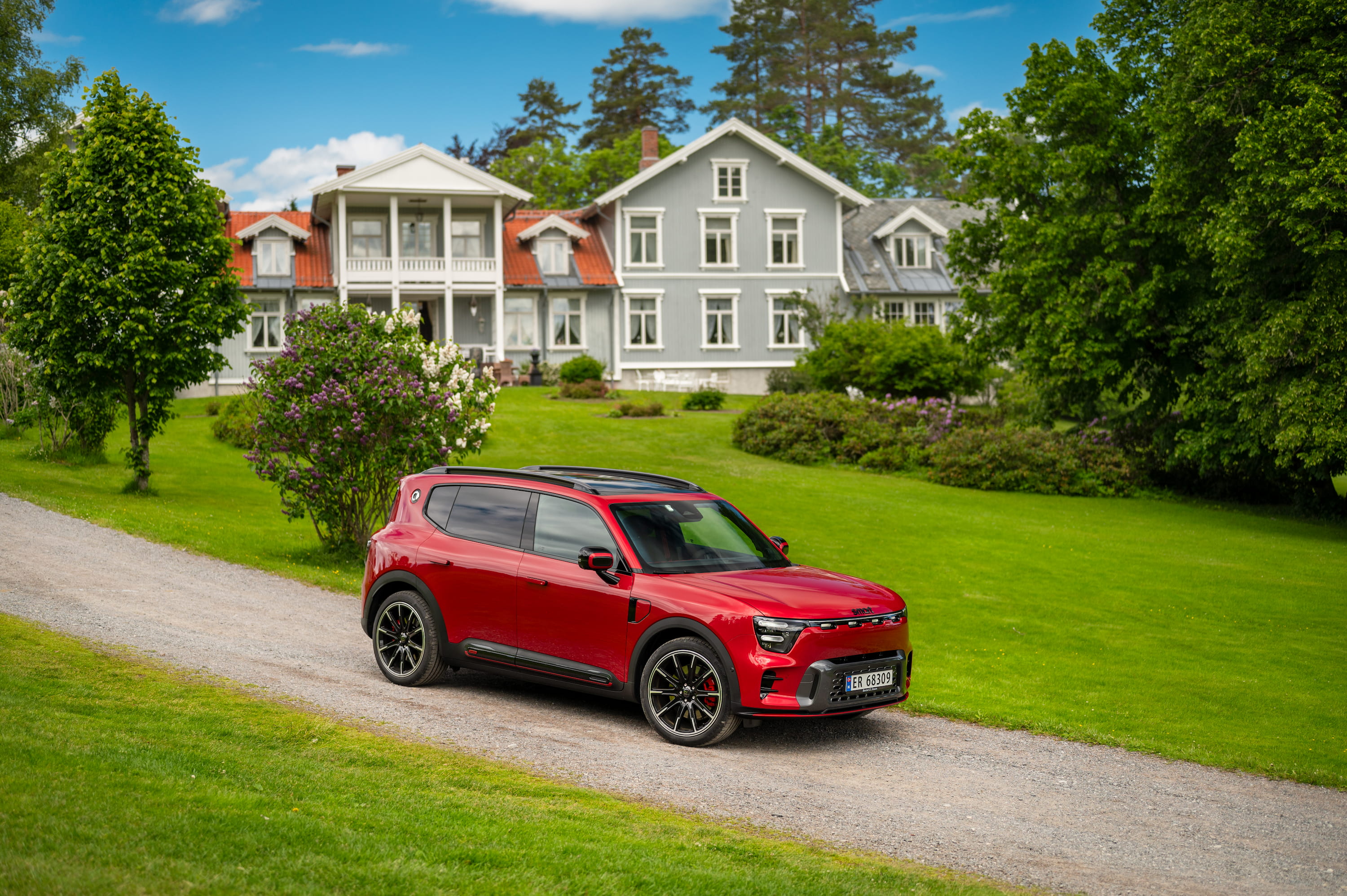 Rød smart #5 BRABUS parkert foran en stor villa med grønn hage