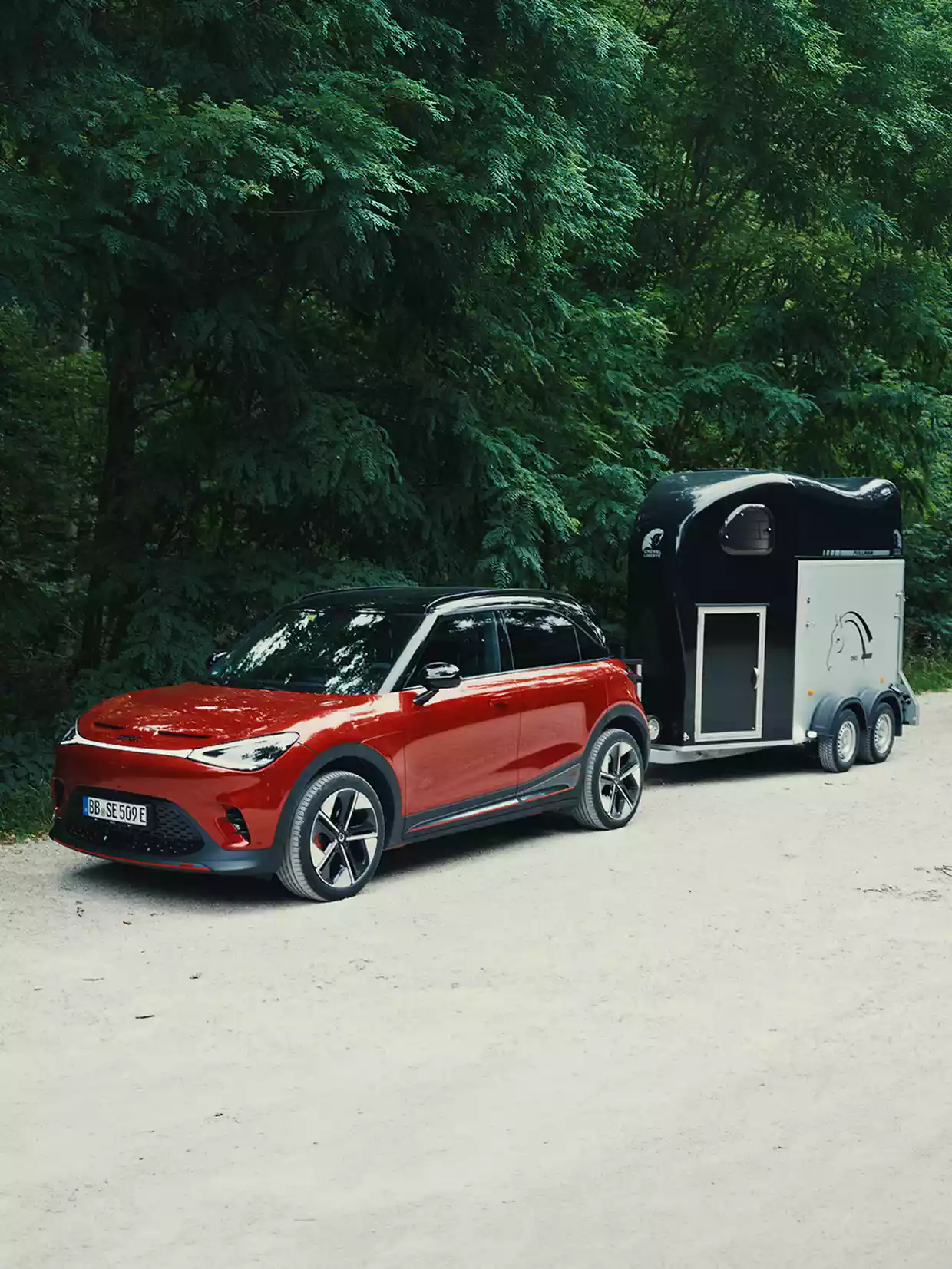 Rød smart #1 med hestehenger på en vei ved skogen