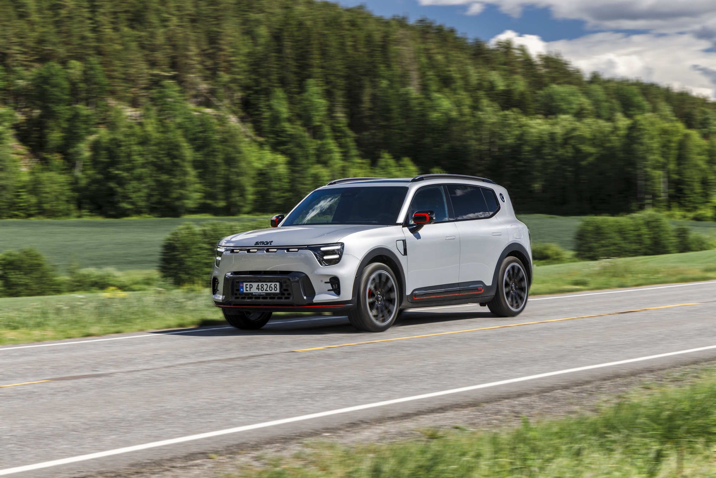 Sølv smart #5 BRABUS kjører på en landevei med skog i bakgrunnen