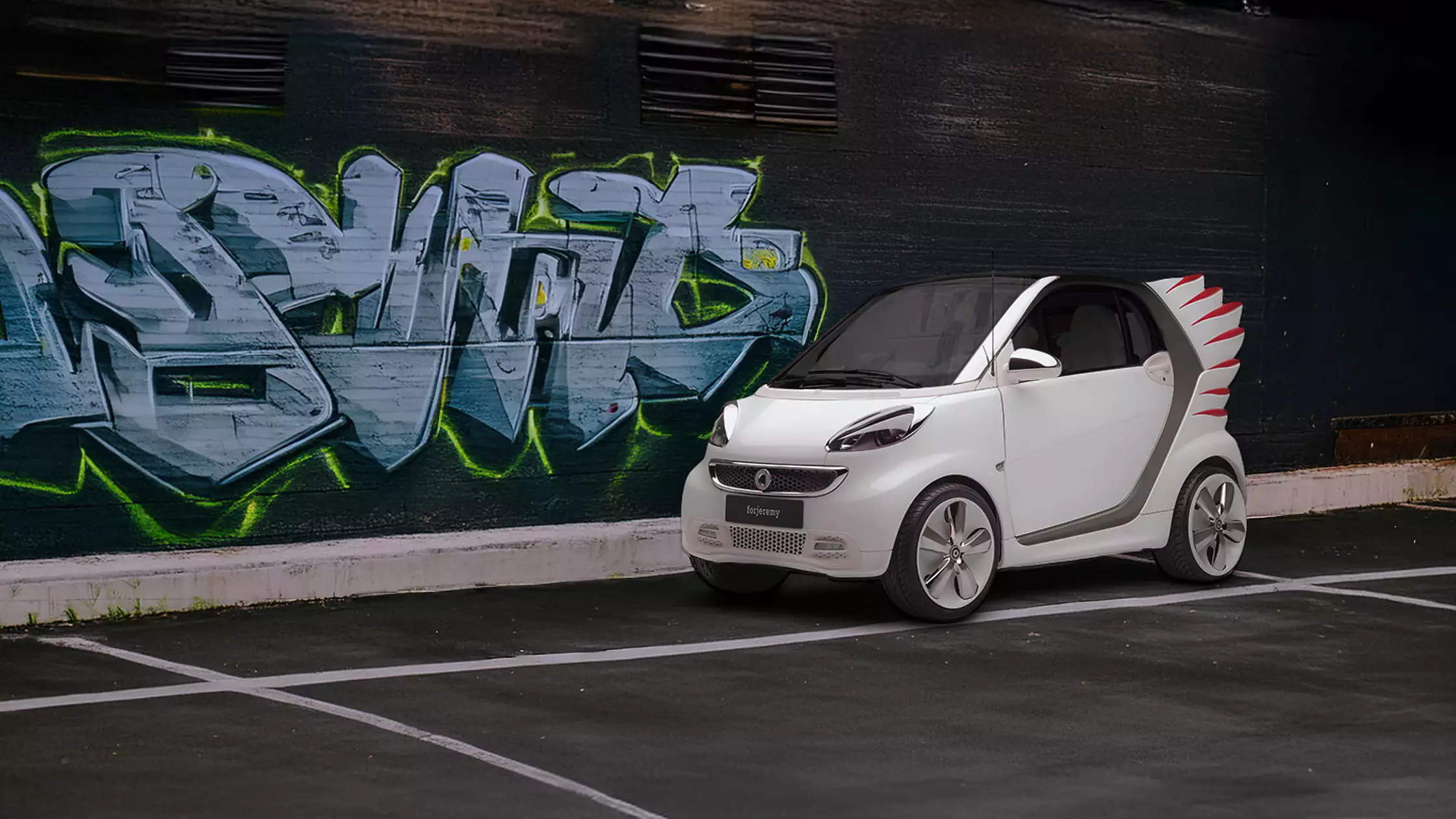 Hvit smart forjeremy parkert foran en graffitivegg