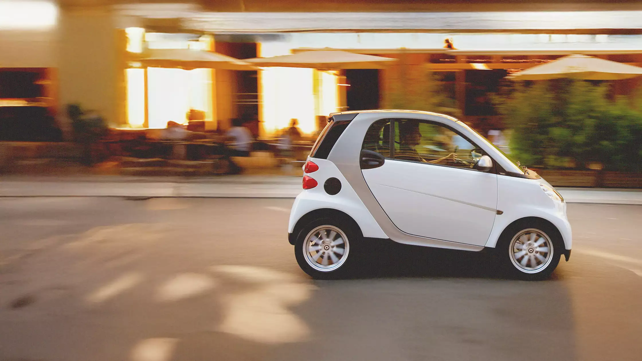 Hvit smart fortwo på vei gjennom en opplyst bygate