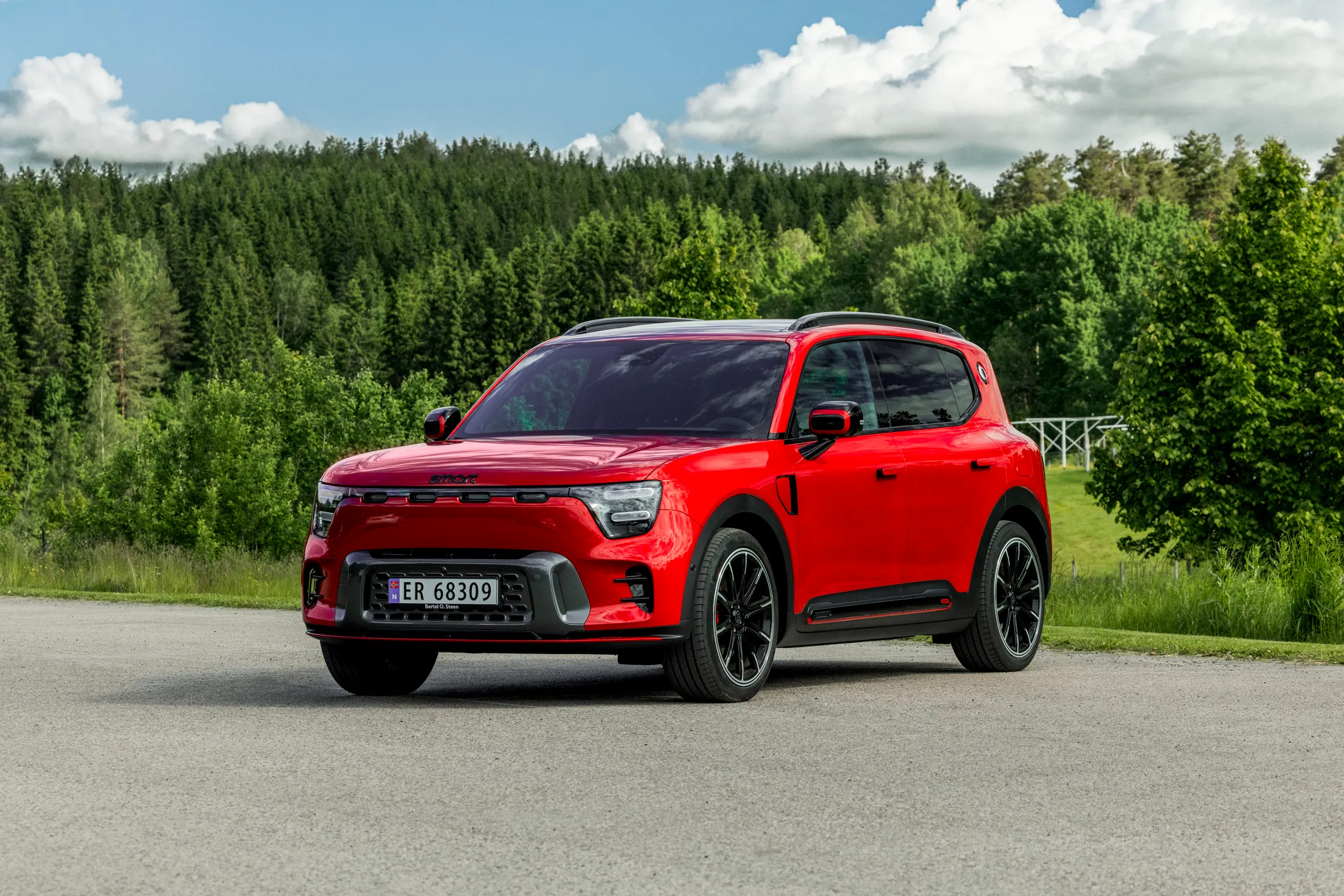Rød smart #5 BRABUS sett skrått forfra på en vei omgitt av grønn natur