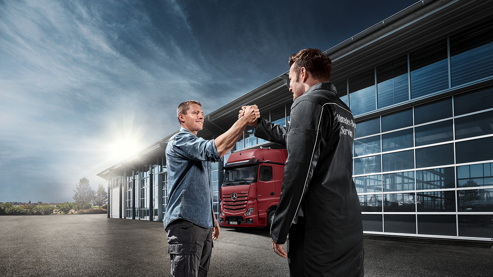 To menn foran en lastebilgarasje som tar hverandre i hånden