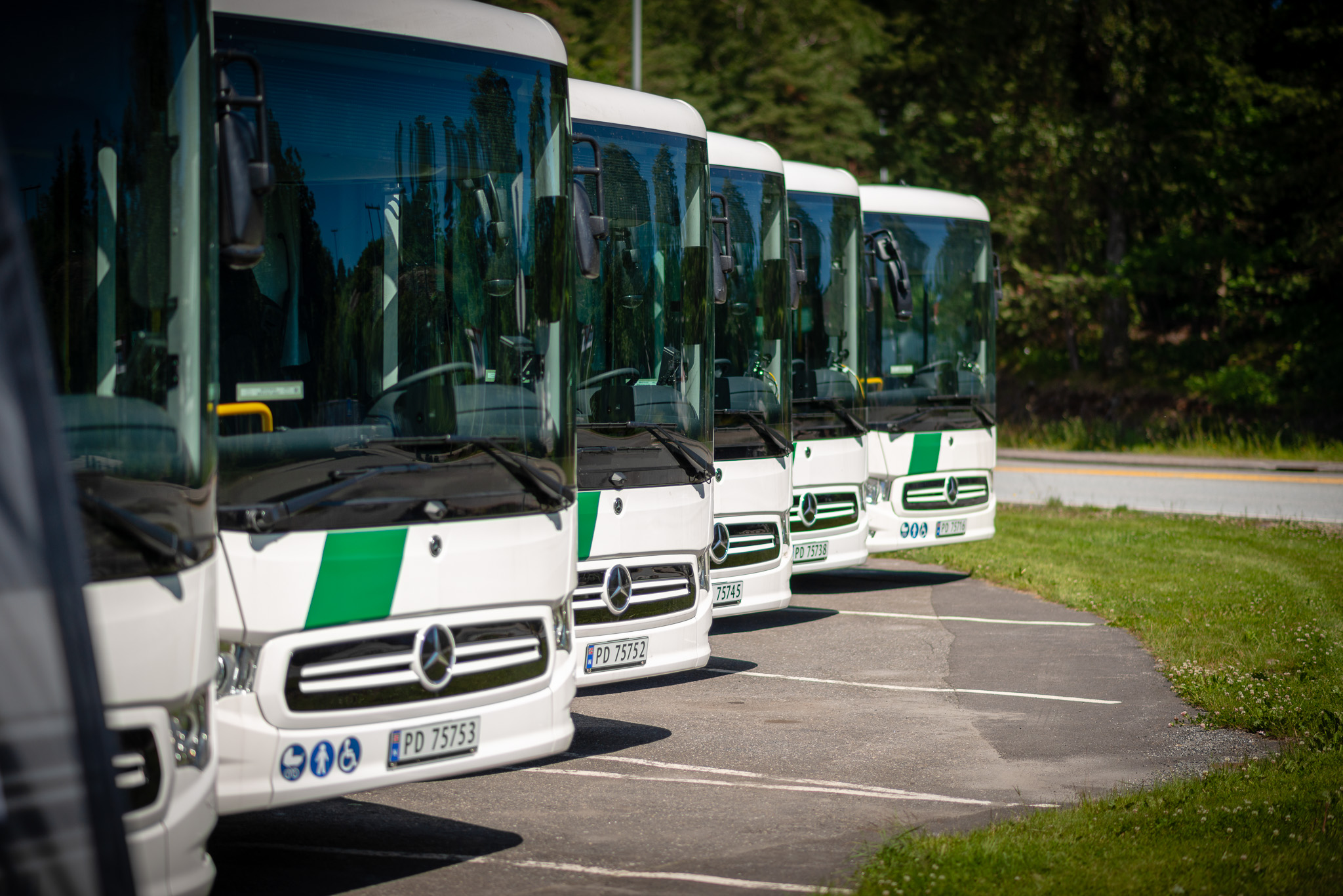 Fotografi av fronten på en rekke Mercedes-Benz Inotouro-busser som står parkert. Bussene er hvite med grønne detaljer.