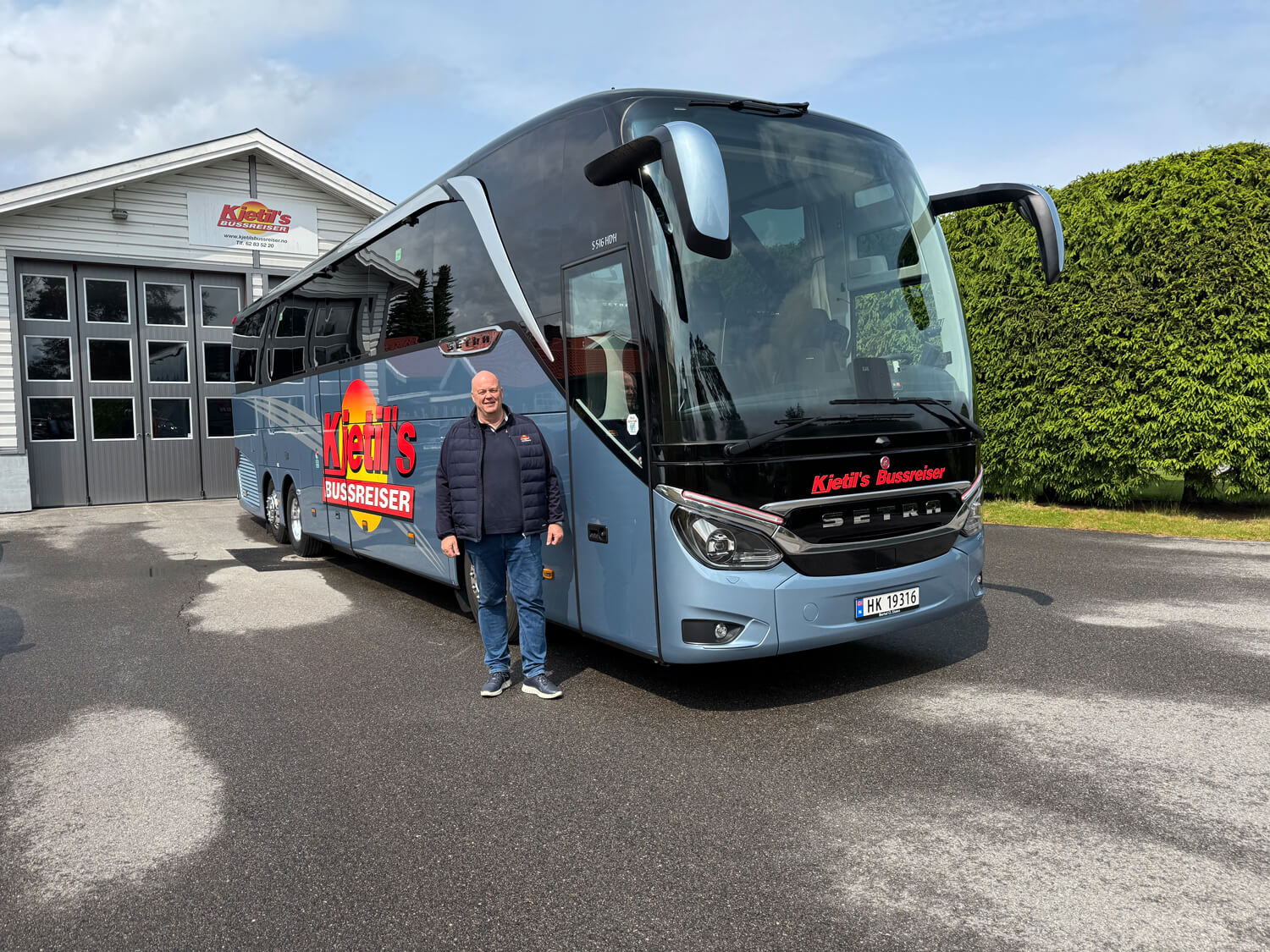 Bilde av mann stående foran en blå buss med logo Kjetils bussreiser