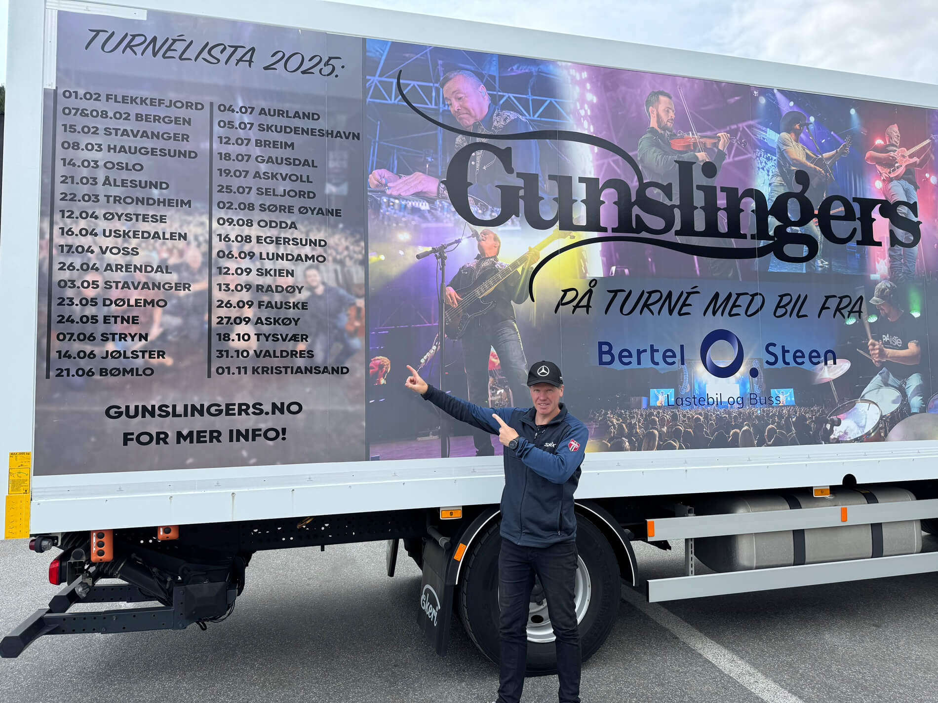 Bilde av mann som står foran en lastebil og peker på turnelisten til bandet Gunslingers