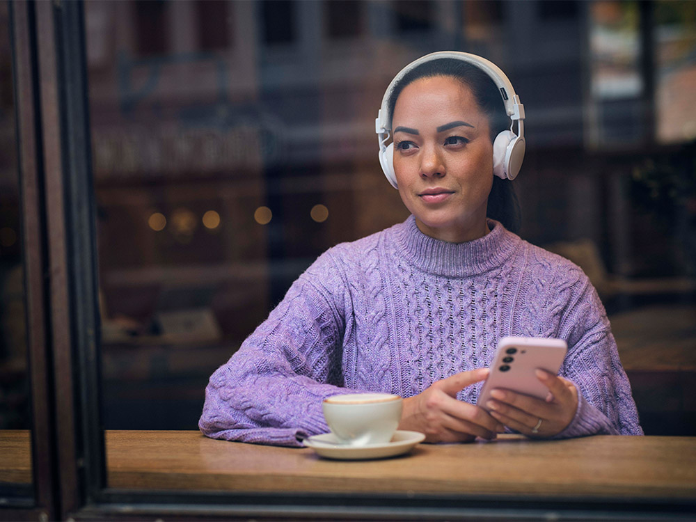 Kvinne hører på lydbok på kafe med hodetelefoner