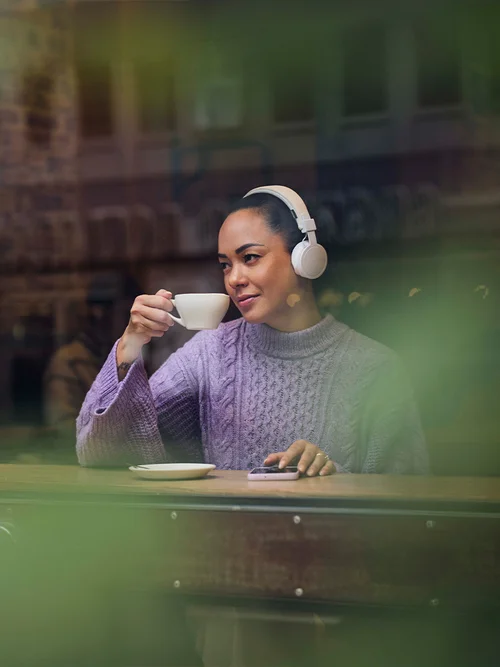 Kvinne drikker kaffe og hører på lydbok på kafe med hodetelefoner