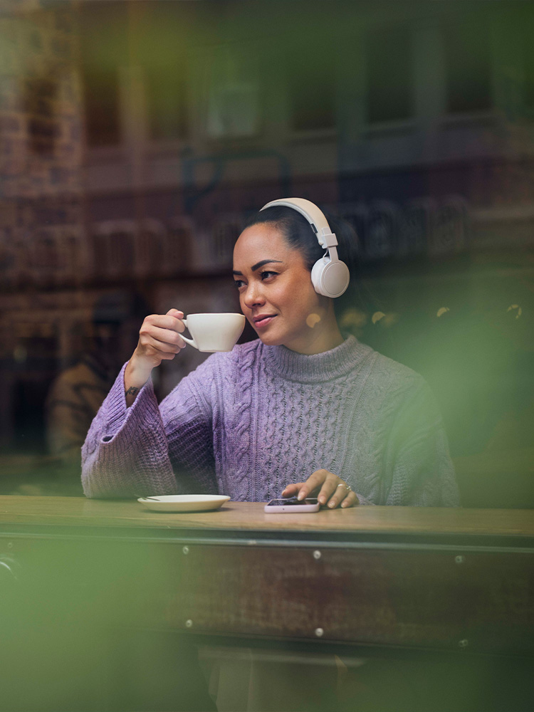Kvinne drikker kaffe og hører på lydbok på kafe med hodetelefoner