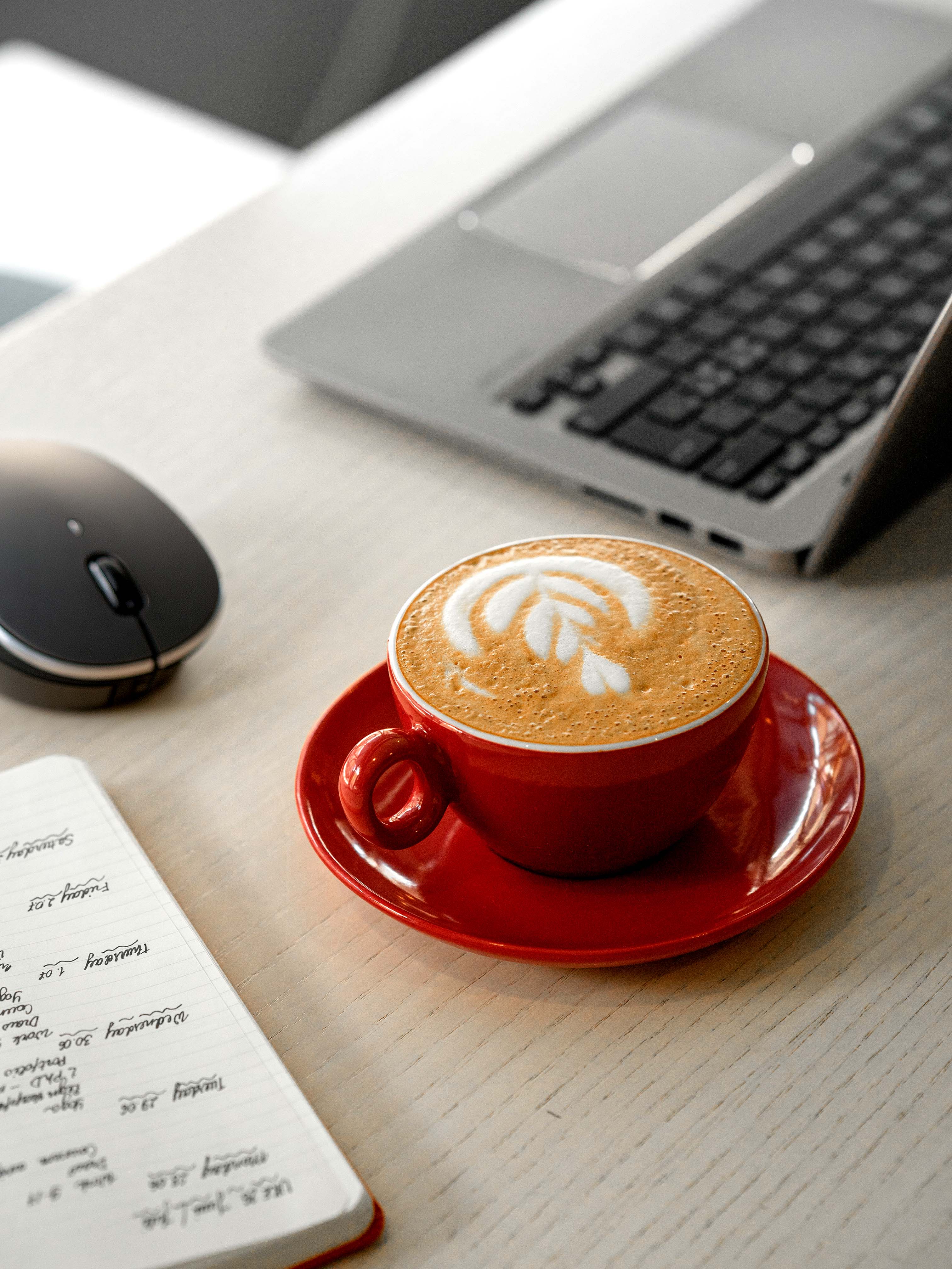 Red coffee mug on table with laptop and notebook