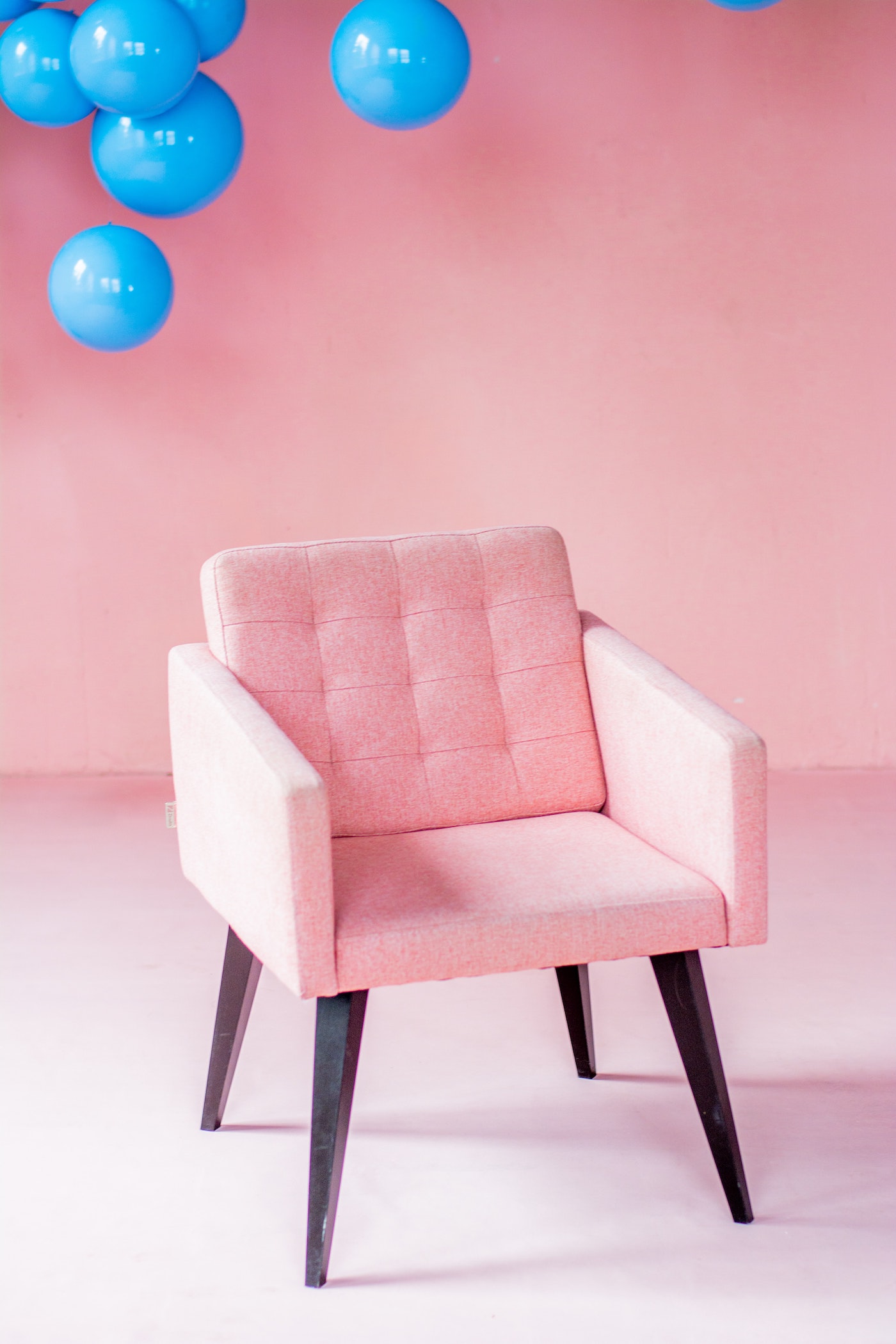 A pink lounge chair with blue balloons in background