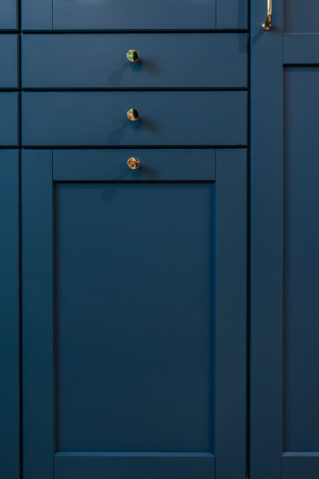 Deep blue framed kitchen fronts and drawers with small brass knobs.