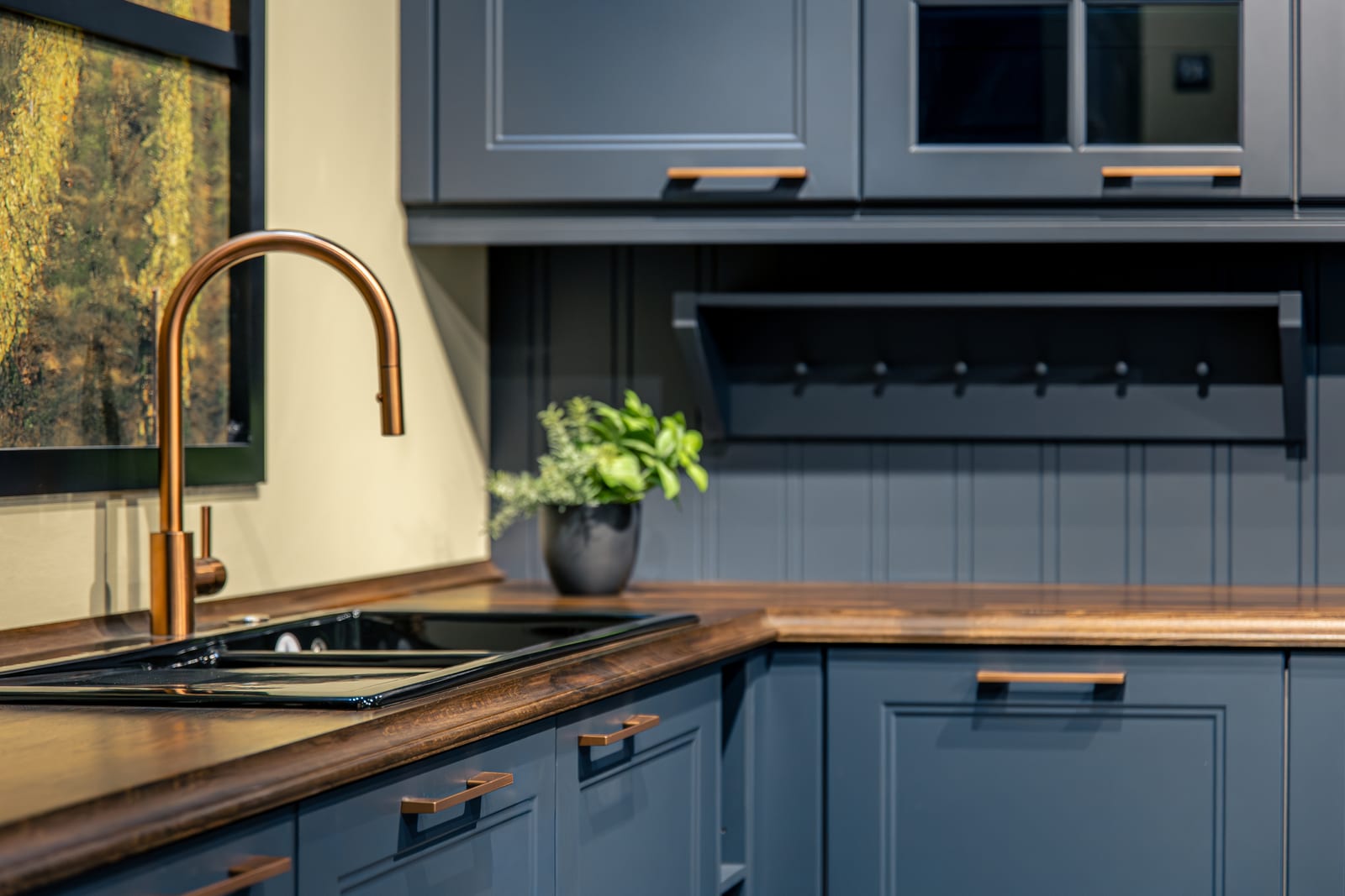 A blue kitchen with a copper tap and a dark wood worktop.
