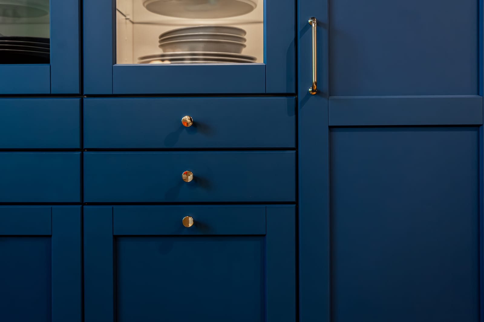 Blue cabinets with brass knobs and a glass-fronted cabinet showing plates.
