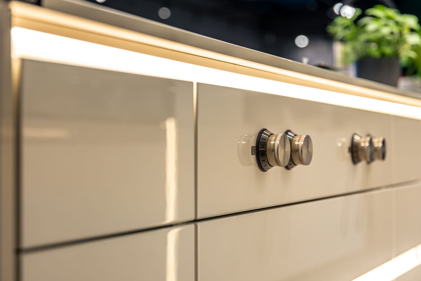 Glossy cream kitchen fronts catching a line of light, with metal knobs.