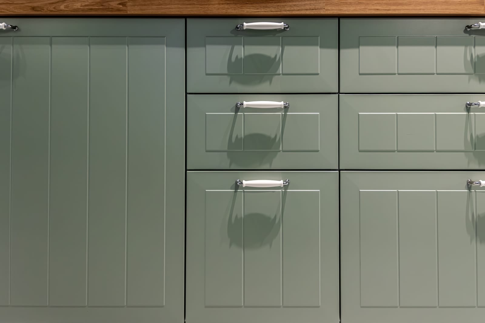 Sage green panelled kitchen fronts with metal handles above a wood worktop.