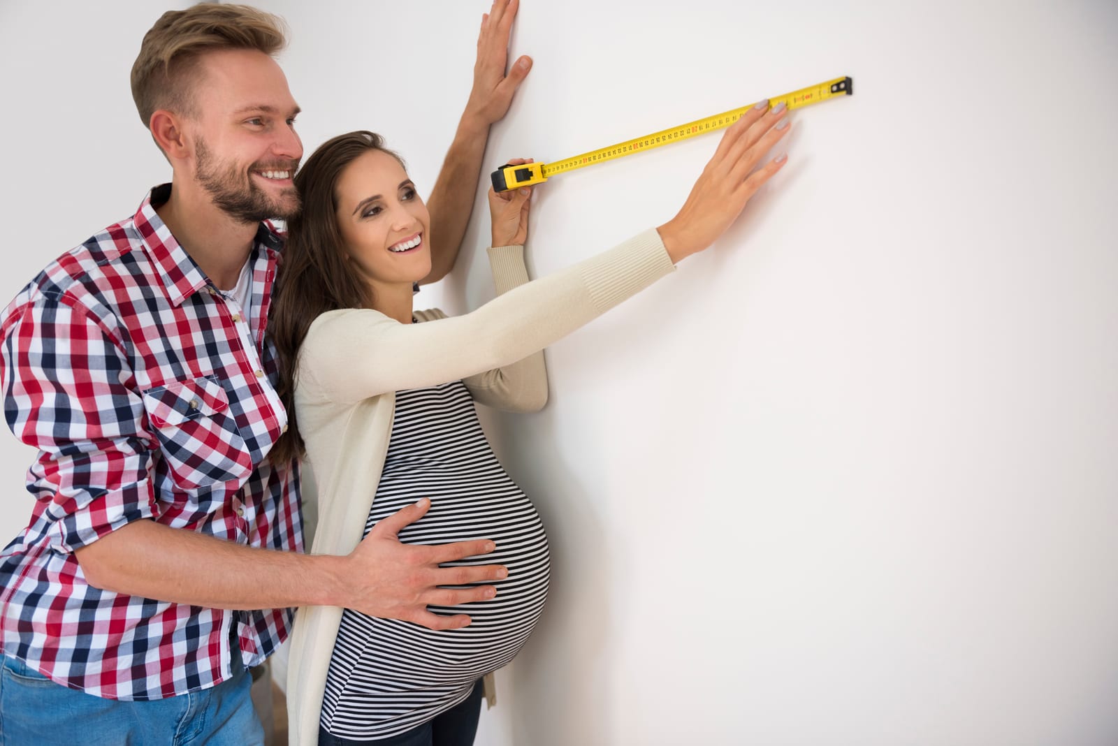 A couple measuring a white wall with a tape measure.