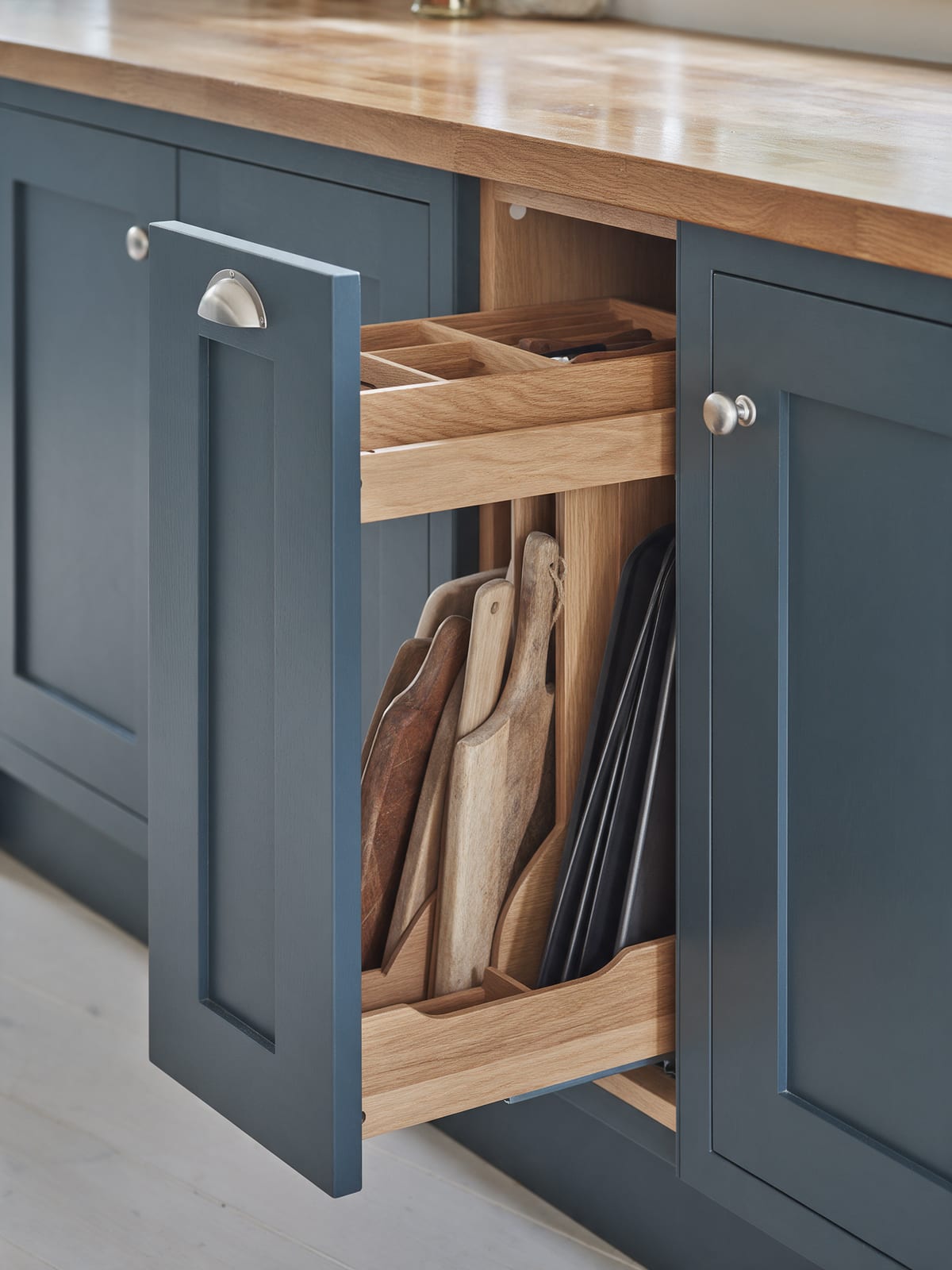 A slim pull-out beside harbour blue fronts with boards and trays stored upright.