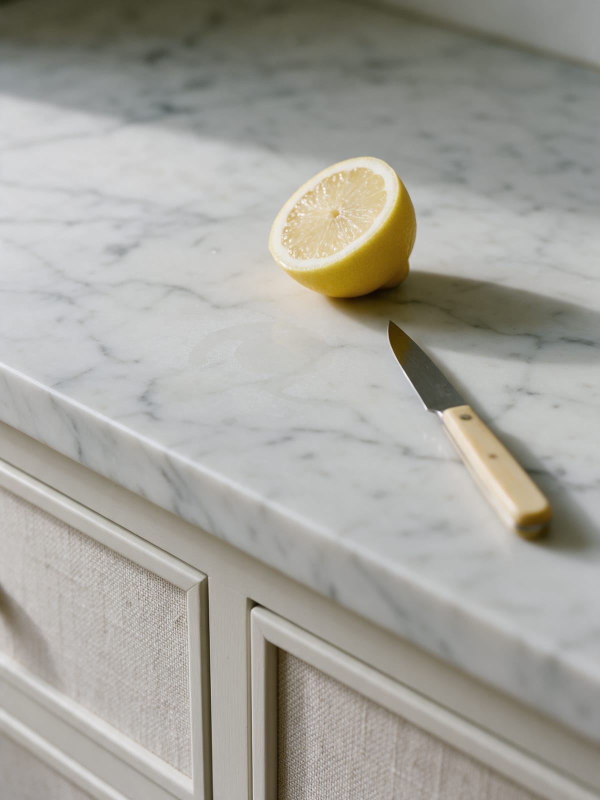 Half a lemon and a knife on honed white marble with a faint etch mark.