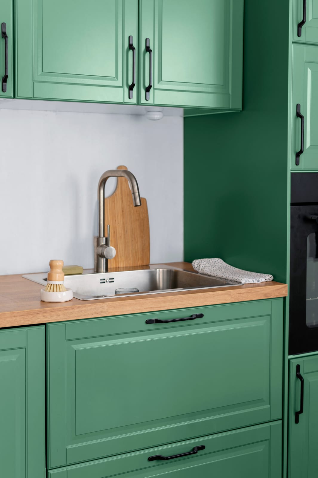A green kitchen with a wooden worktop, a sink and a brass tap.