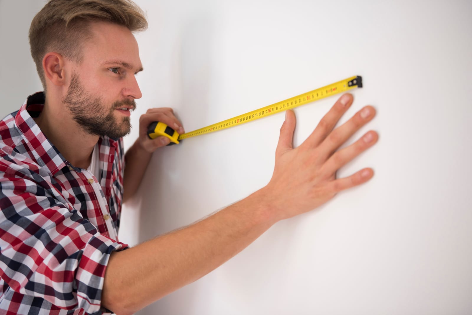 Measuring the width of an empty wall with a tape measure.