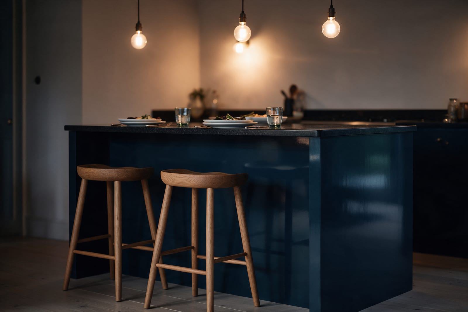 An ink-blue island in the evening under globe pendant lights, with two oak stools.
