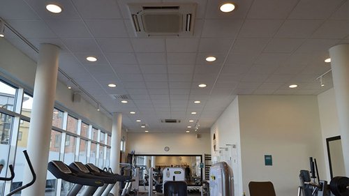 Interiör av ett gym med träningsmaskiner och stora fönster som släpper in naturligt ljus. I taket finns Mitsubishi Electrics klimataggregat för att säkerställa en behaglig inomhusmiljö under träning.