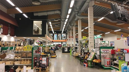 Interiör av Hörby Lantmäns butik, med hyllor fyllda av varor som trädgårdsredskap, djurprodukter och verktyg. Tydlig belysning och synlig ventilationsanläggning i taket bidrar till butikens moderna design.