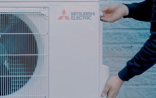 En person utför service på en Mitsubishi Electric utomhusenhet för luftkonditionering. Det betonar vikten av regelbunden service för att säkerställa optimal prestanda och förebygga problem.