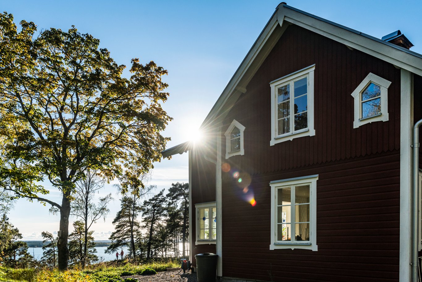 Röd villa vid en sjö i motljus en sommardag, vilket illustrerar Mitsubishi Electrics fokus på hållbarhet och kvalitet i konstruktion och hantverk.