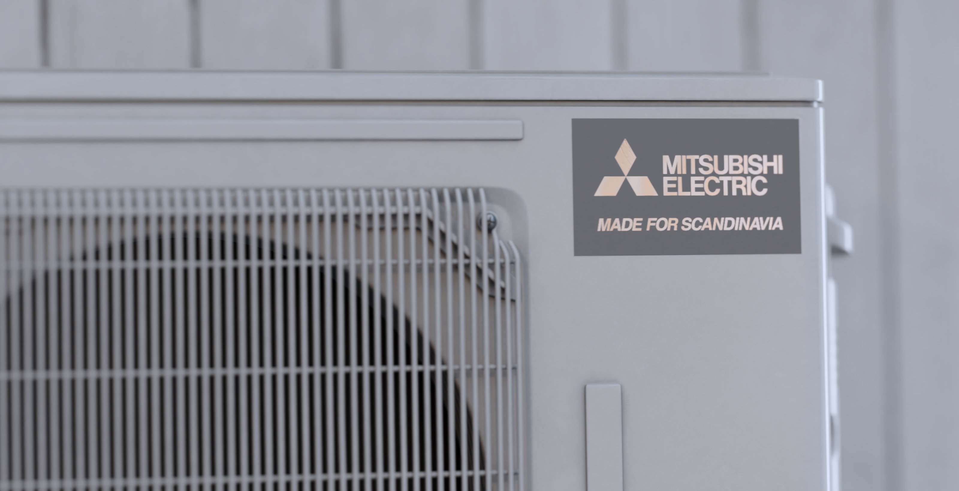 Mitsubishi Electrics utomhusenhet med märkningen "Made for Scandinavia," som betonar hållbarhet och effektivitet designad för tuffa nordiska förhållanden. Enheten är monterad mot en ljus vägg och illustrerar ett engagemang för hållbara värmelösningar.