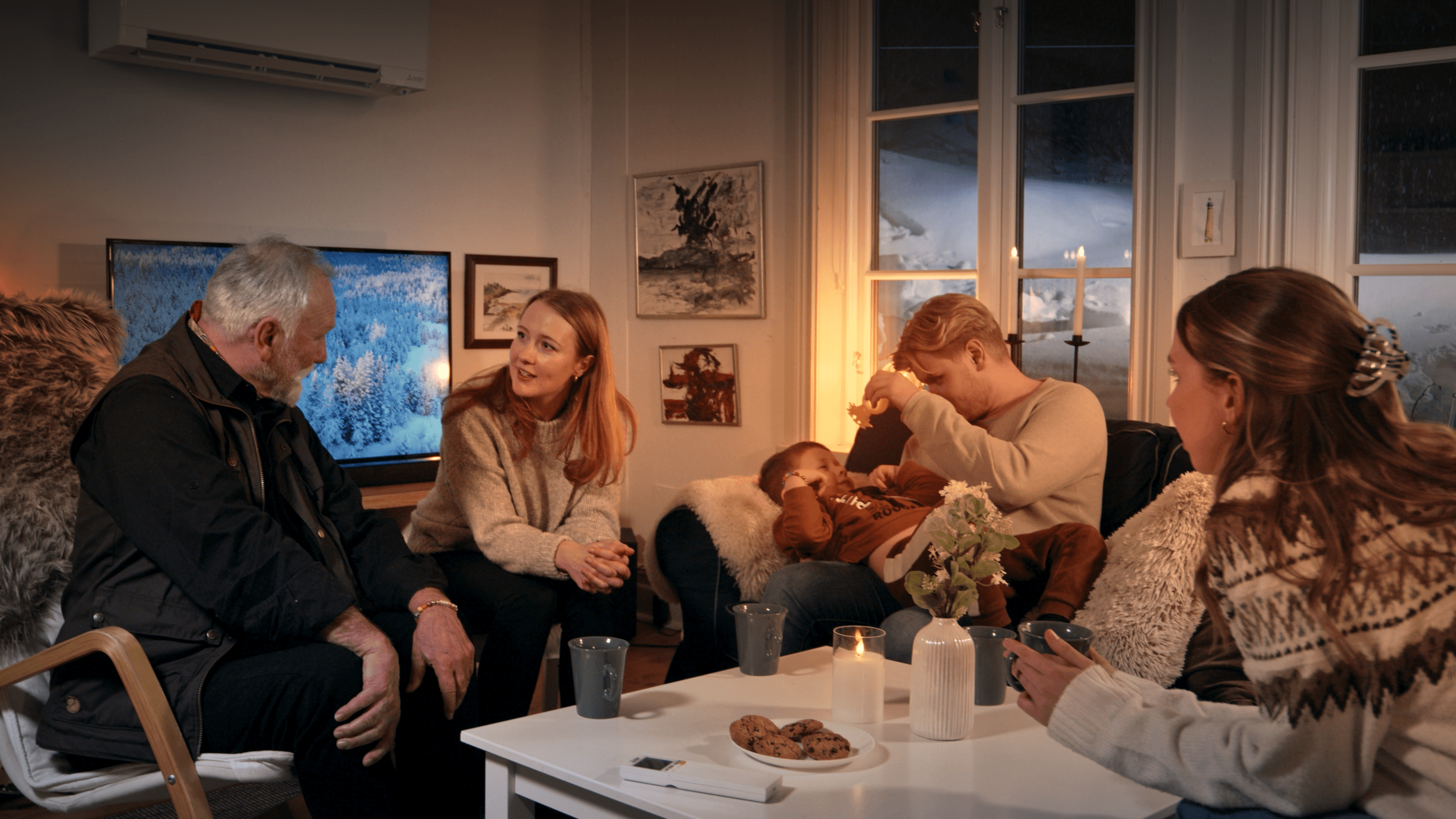 Varmt belyst vardagsrum där en familj samlas kring en Mitsubishi Electric värmepump, vilket illustrerar företagets fokus på energieffektiv och hållbar värme för skandinaviska hem genom märkningen Made for Scandinavia.