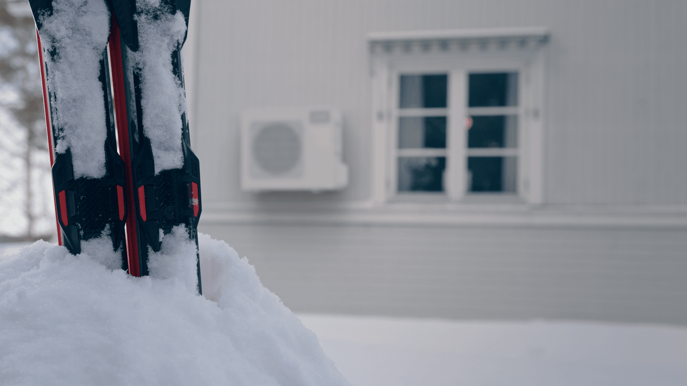 Snötäckta skidor framför en utomhusenhet från Mitsubishi Electric på en fasad, som visar företagets fokus på värmesystem som fungerar tillförlitligt även i kalla skandinaviska vintrar.