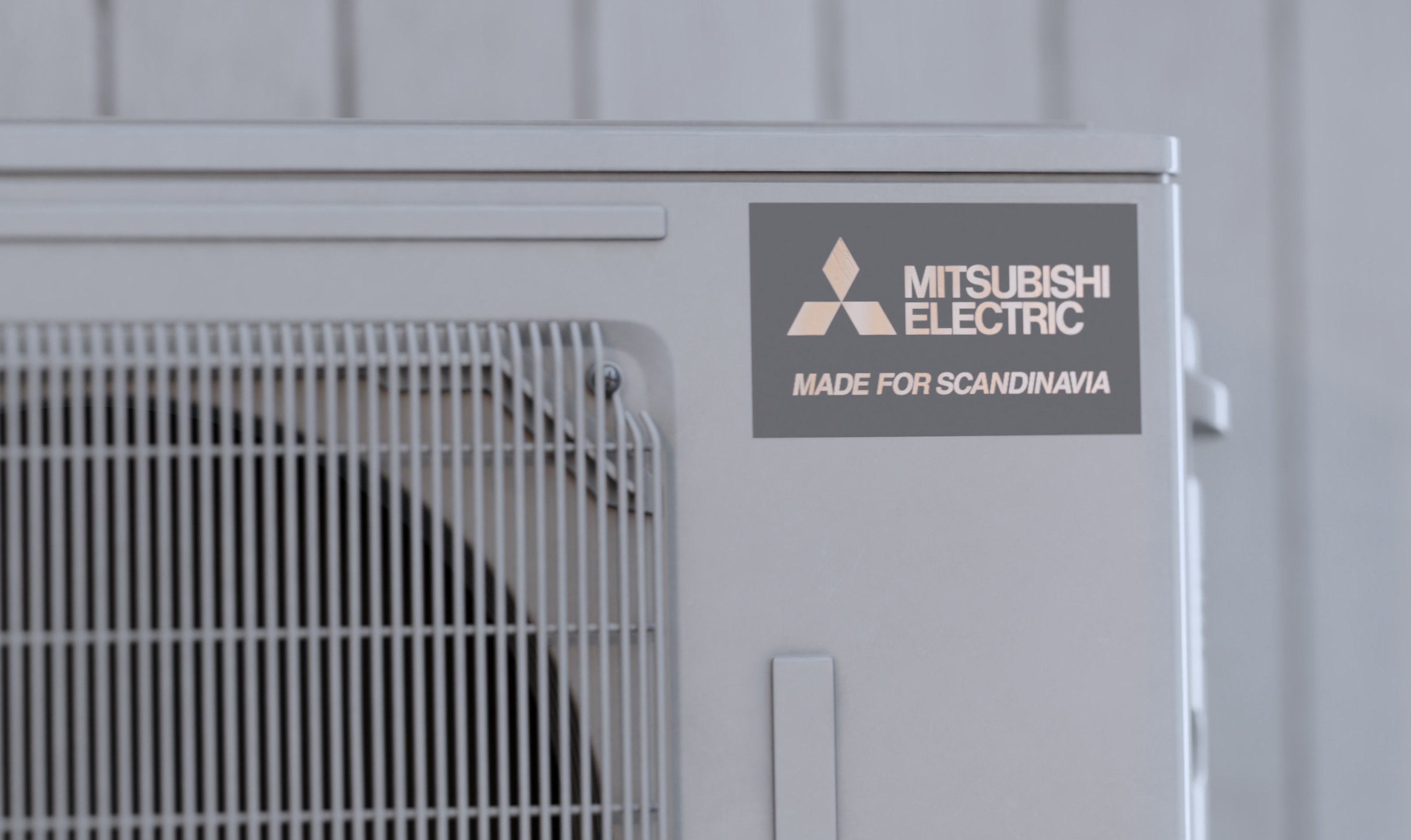 Mitsubishi Electrics utomhusenhet med märkningen Made for Scandinavia, som betonar hållbarhet och effektivitet designad för tuffa nordiska förhållanden. Enheten är monterad mot en ljus vägg och illustrerar ett engagemang för hållbara värmelösningar.