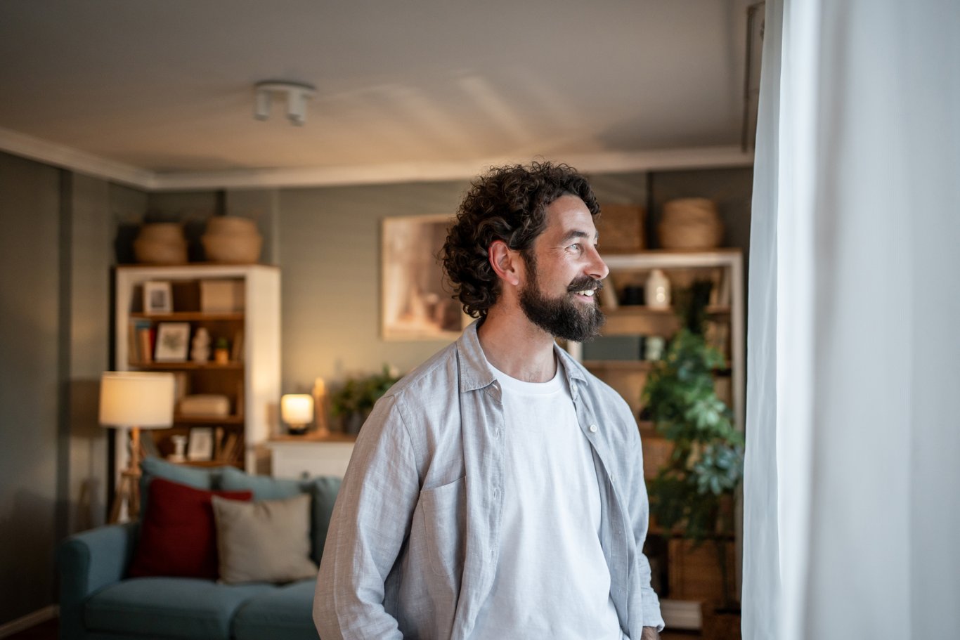 Man står i ett ombonat vardagsrum och tittar ut genom fönstret. 